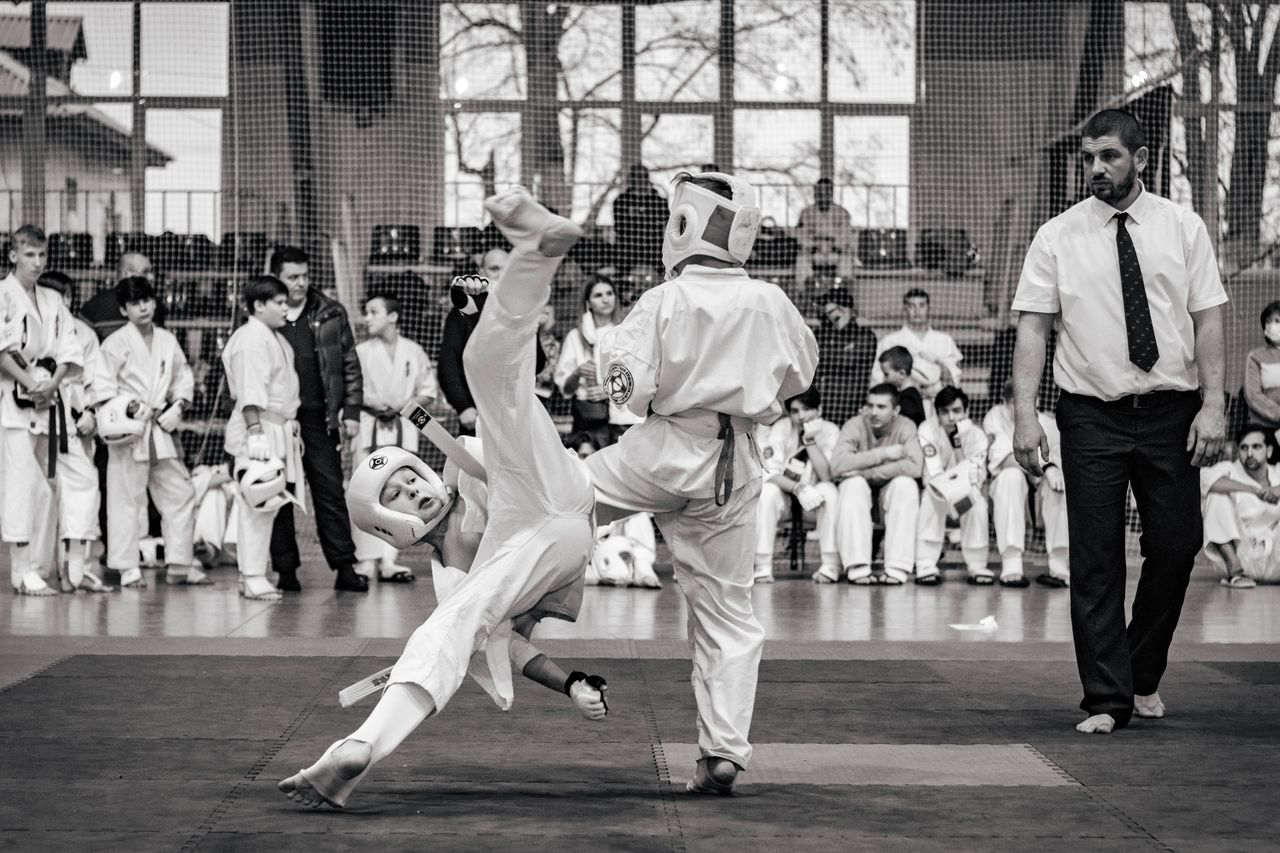 Martial artists sparring during a competitive karate event with a focused referee.