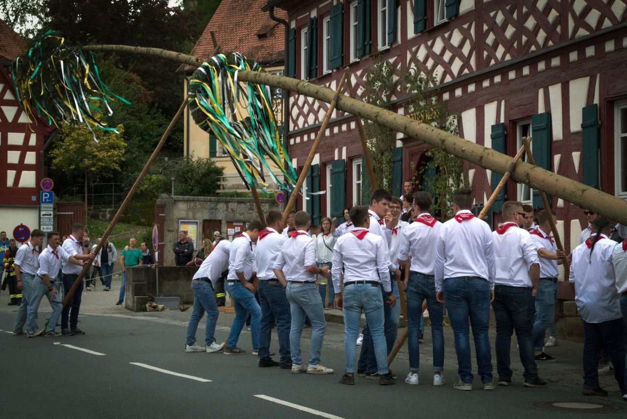 Men in traditional attire participate in a Bavarian maypole setup in Großhabersdorf, Germany, showcasing cultural heritage.