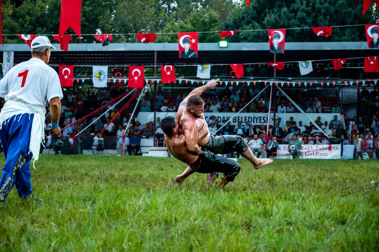 Exciting oil wrestling match with spectators and Turkish flags on display.