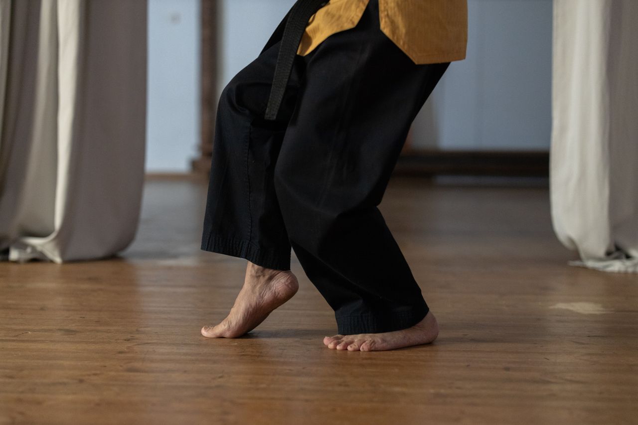 Person practicing martial arts barefoot on a wooden floor indoors.